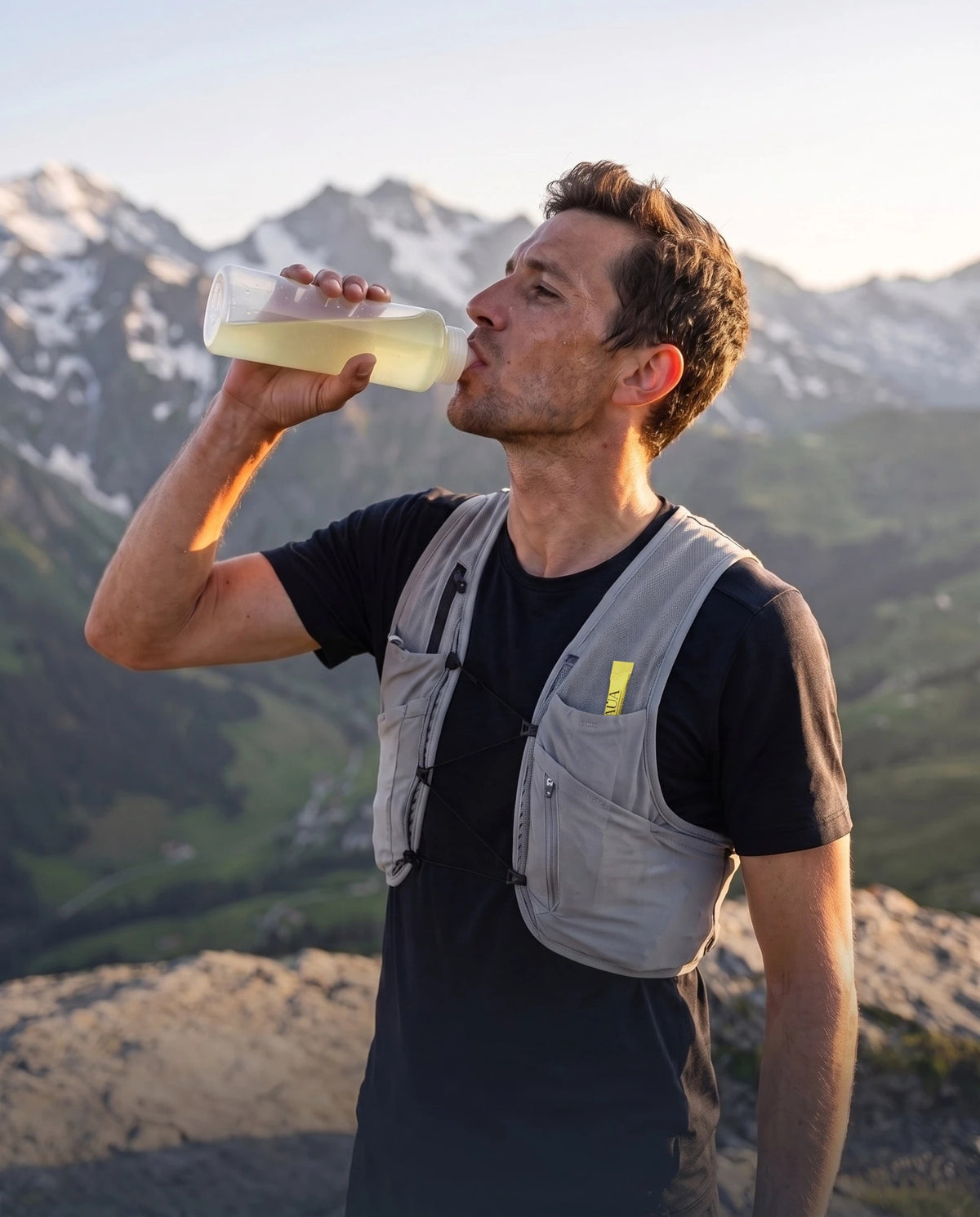 Traileur qui boit AUA Hydrate citron dans une gourde transparente, en montagne